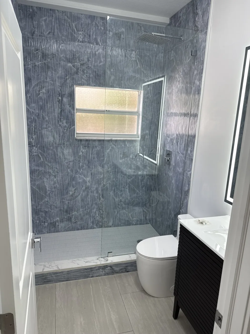 Completed bathroom with blue shower tile, glass shower panel, installed shower fixtures, gray flooring and dark vanity
