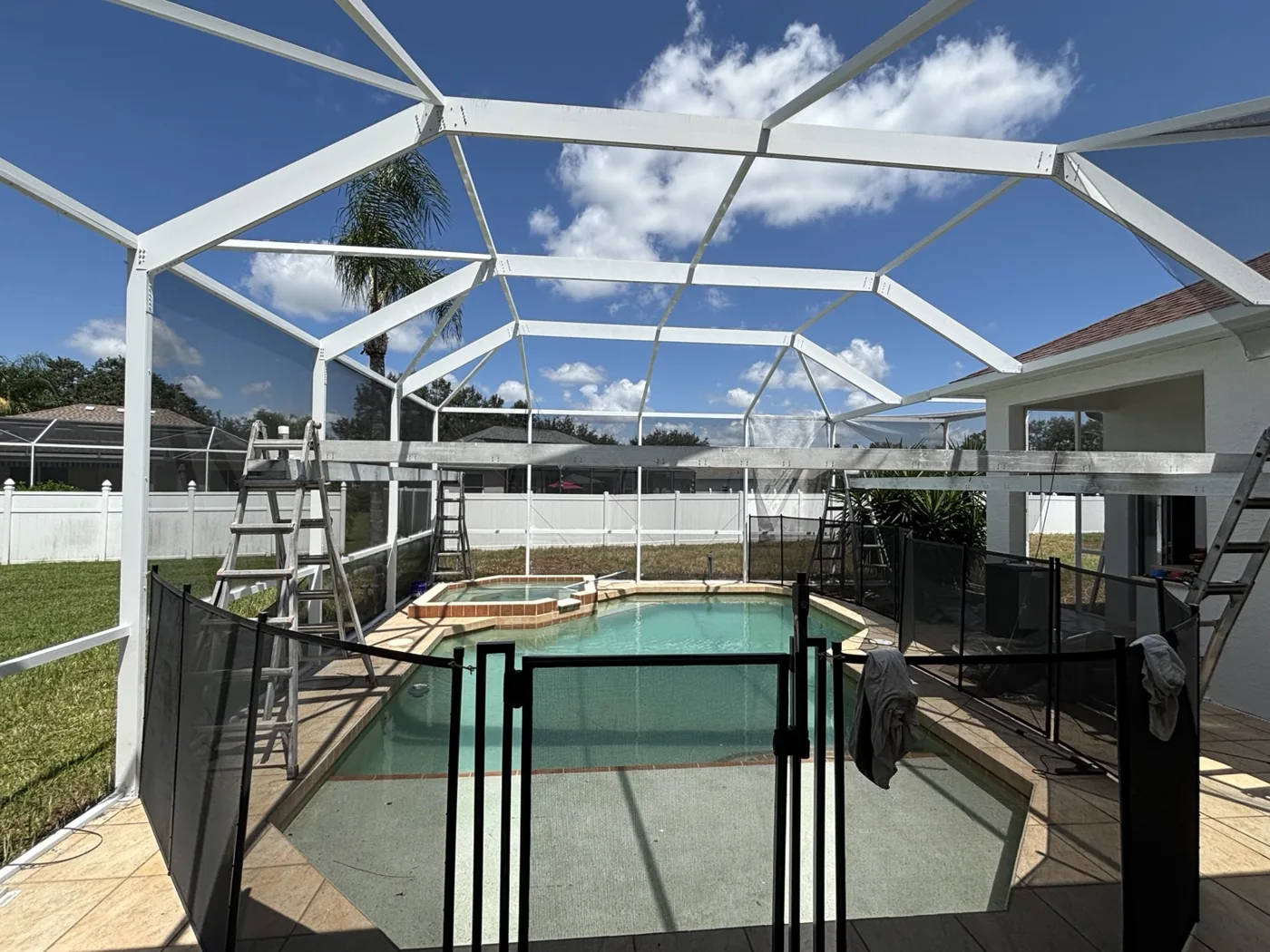 Pool enclosure with screening removed and ladders in place during preparation